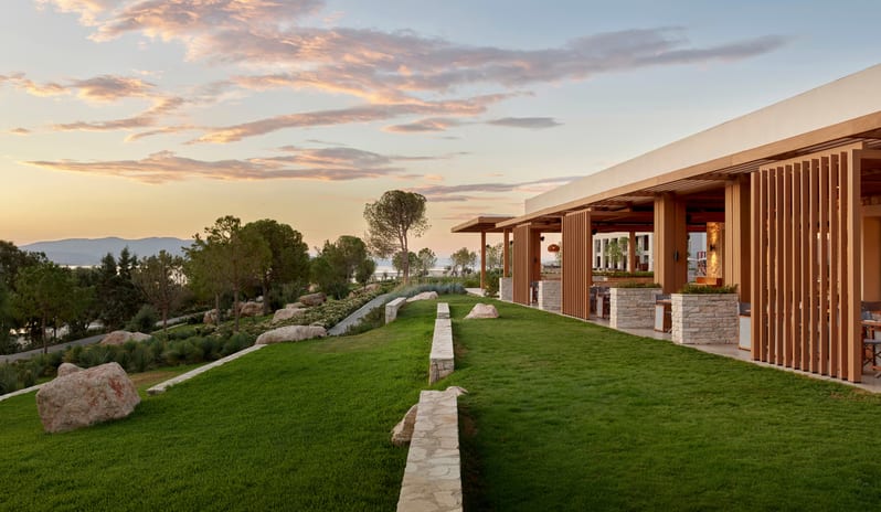Mansion Restaurant International Kitchen natural stone retaining walls, wooden pergolas, and a tiered green lawn with large decorative boulders under a bright sky at Anda Barut Collection by Kenwood Travel
