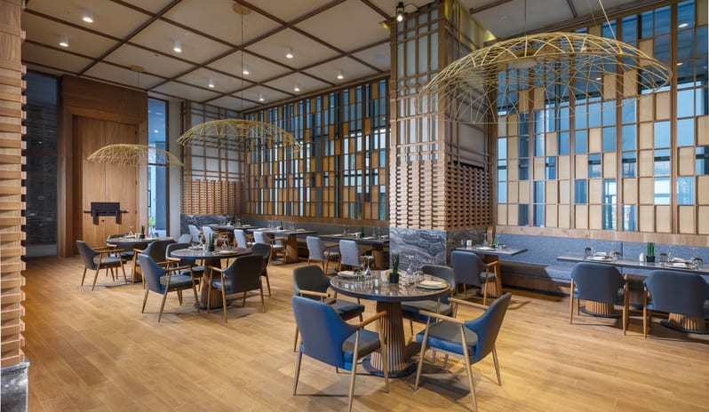 Tiger Restaurant dining area with warm wood tones, architectural grid ceilings, and stylish gold pendant lamps at Anda Barut Collection by Kenwood Travel