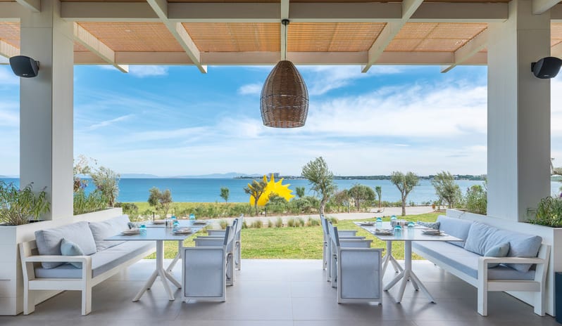 Fish Camp Restaurant outdoor restaurant terrace with white wooden dining tables, woven basket pendant lights, and a coffered ceiling offering a panoramic view of the blue ocean and coastline at Anda Barut Collection by Kenwood Travel