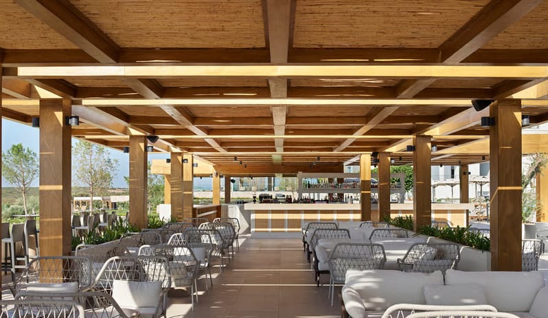 Community Pool Bar outdoor hotel bar featuring a bamboo slat ceiling, wooden pergola, and white contemporary wicker seating at Anda Barut Collection by Kenwood Travel