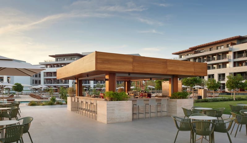 Family Pool Bar open-air wooden pool bar with green seating at a luxury hotel resort during sunset at Anda Barut Collection by Kenwood Travel