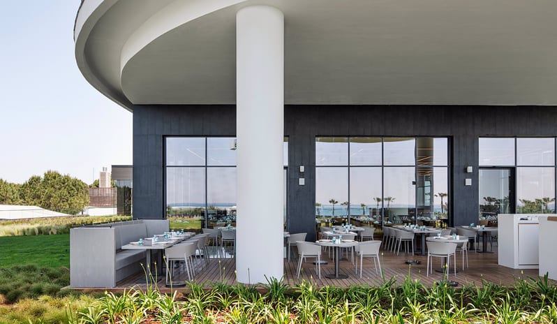 Degusto Adult Restaurant featuring minimalist furniture, wooden decking, and a view of the Mediterranean greenery at Voyage Belek Golf & Spa by Kenwood Travel