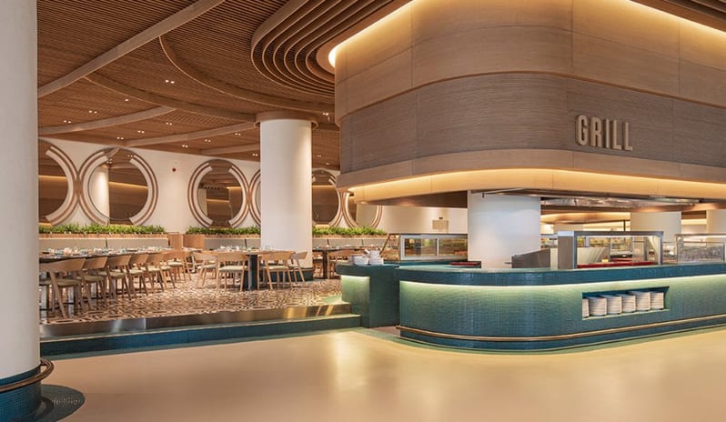 Degusto Main Restaurant circular grill station with teal mosaic tiling, a distinctive slatted wooden ceiling design, and a spacious dining area with elegant round mirrors at Voyage Belek Golf & Spa by Kenwood Travel