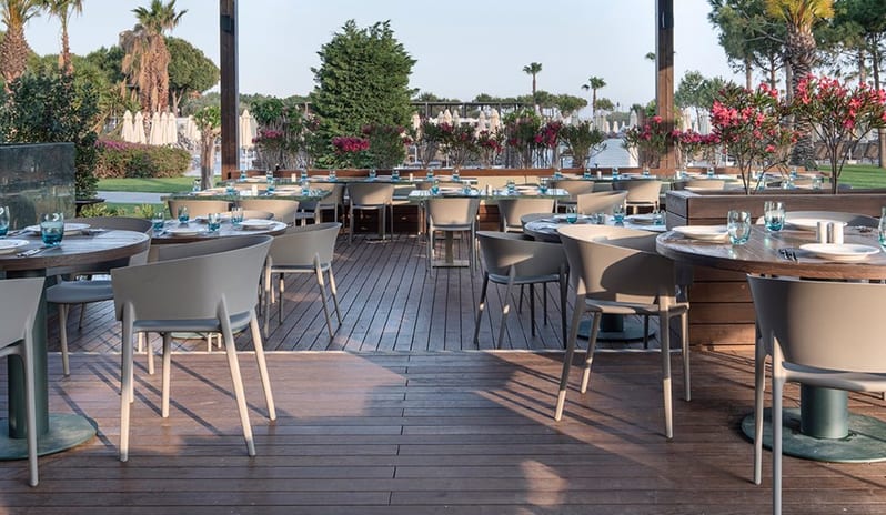Degusto Main Restaurant Outdoor patio seating at Voyage Belek Golf & Spa Degusto Main Restaurant, showing contemporary furniture design and tropical landscaping in Belek, Turkey at Voyage Belek Golf & Spa by Kenwood Travel