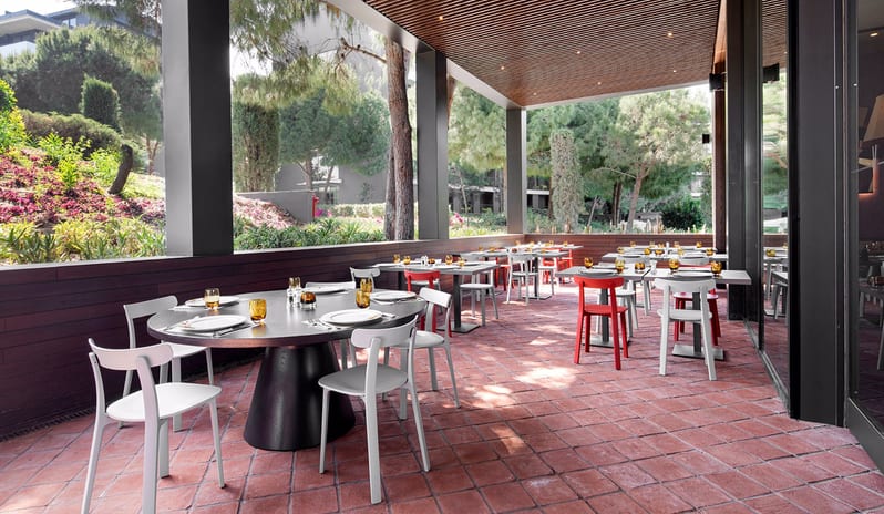 Gracias Mexican Restaurant red and white modern chairs, terracotta tile flooring, and a view of lush garden greenery at Voyage Belek Golf & Spa by Kenwood Travel