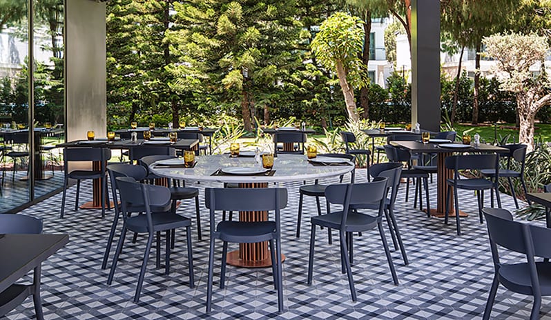 Kebappa Turkish Restaurant blue modern chairs, marble-topped tables, and a distinctive geometric tiled floor surrounded by pine trees at Voyage Belek Golf & Spa by Kenwood Travel