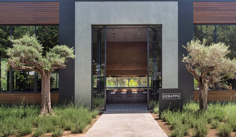 Kebappa Turkish Restaurant exterior entrance of Kebappa Kebab and Grill at Voyage Belek Golf and Spa featuring olive trees and a minimalist facade at Voyage Belek Golf & Spa by Kenwood Travel