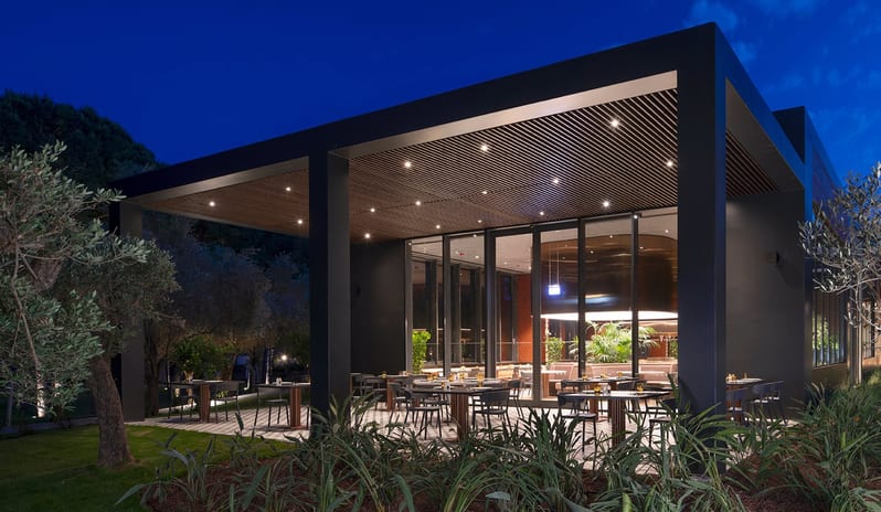 Kebappa Turkish Restaurant modern architecture with a wooden slatted ceiling, warm spotlights, and outdoor tables under a dark blue twilight sky at Voyage Belek Golf & Spa by Kenwood Travel