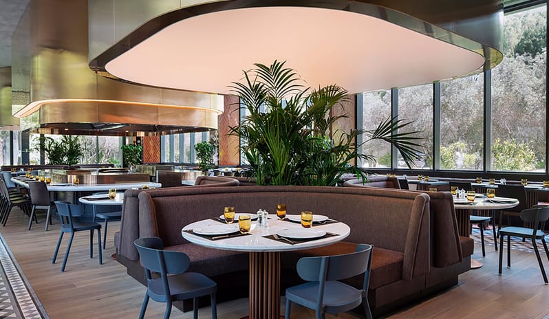 Kebappa Turkish Restaurant circular booth seating, modern pendant lighting, and large windows overlooking lush greenery at Voyage Belek Golf & Spa by Kenwood Travel