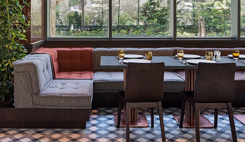 Kebappa Turkish Restaurant gray and terracotta tufted cushions, dark wood chairs, and large windows with a garden view at Voyage Belek Golf & Spa by Kenwood Travel