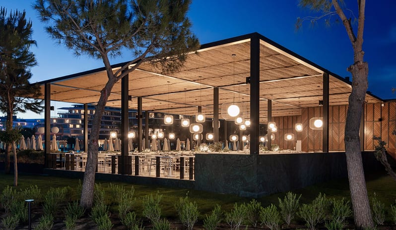 Vista Italian Restaurant featuring glowing globe pendant lights, a textured canopy roof, and evening ambient lighting at Voyage Belek Golf & Spa by Kenwood Travel