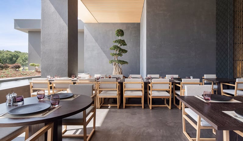 Wen Chinese Restaurant dark wood tables, a decorative bonsai tree against a grey wall, and views of the resort greenery at Voyage Belek Golf & Spa by Kenwood Travel
