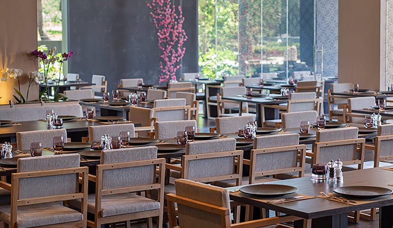 Wen Chinese Restaurant dark wood tables, grey upholstered chairs, and pink floral accents near large windowsat Voyage Belek Golf & Spa by Kenwood Travel