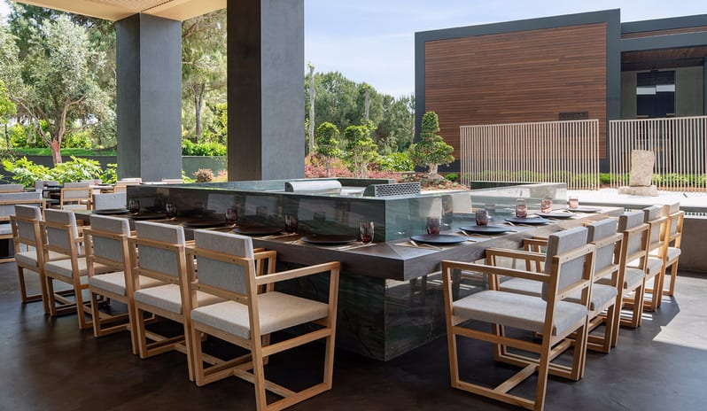 Wen Teppanyaki Japanese Restaurant minimalist wooden chairs, dark tables, and a view of lush green gardens at Voyage Belek Golf & Spa by Kenwood Travel