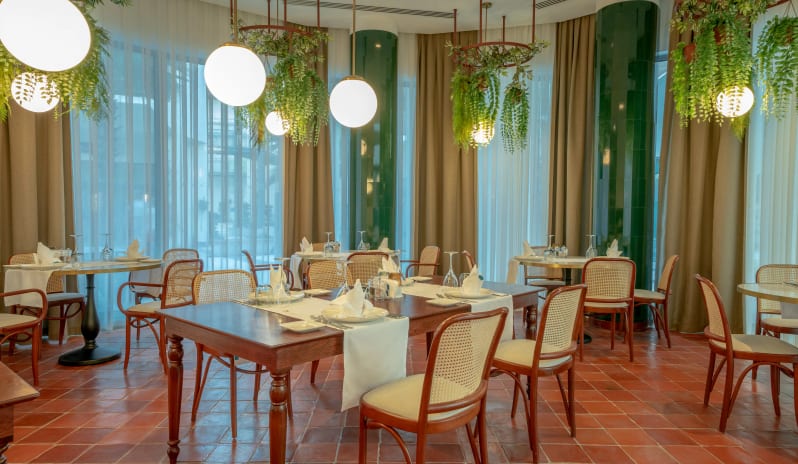 Balbura Italian Restaurant terracotta tile flooring, bentwood cane chairs, and hanging greenery with globe pendant lighting at Liberty Fabay by Kenwood Travel