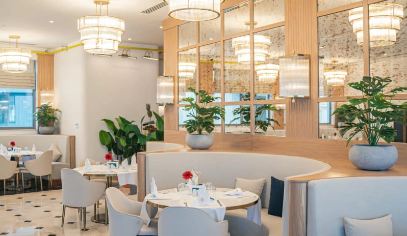 Myros Adults Main Restaurant featuring curved beige booths, marble floors with black accents, and tiered glass chandeliers at Liberty Fabay by Kenwood Travel