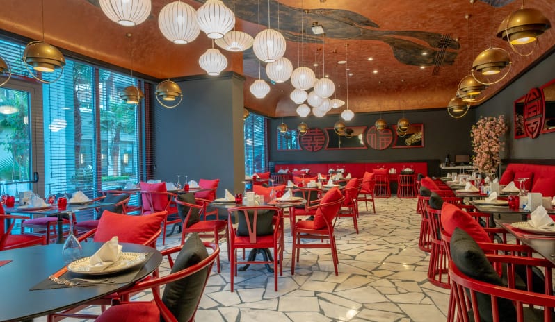 Nysa Asia Restaurant red upholstered chairs, black tables, and decorative white paper lantern lighting at Liberty Fabay by Kenwood Travel