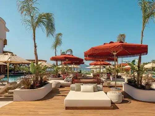 Breeze Bar white daybeds, terracotta umbrellas, and palm trees under a clear blue sky at Liberty Signa Hotel by Kenwood Travel