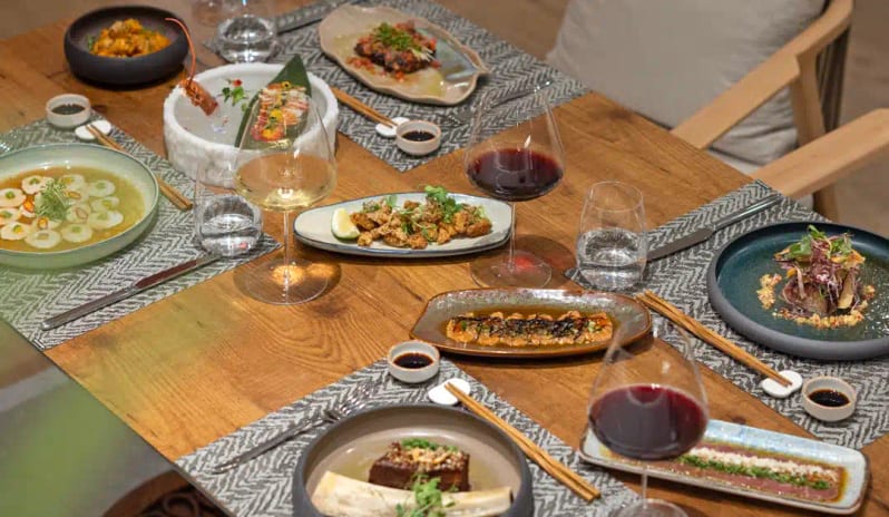 Miyabi A’la Carte Restaurant assorted sushi, gourmet appetizers, red wine, and traditional place settings on a wooden table at Liberty Signa Hotel by Kenwood Travel