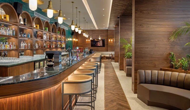 Grano Pub curved marble countertop, arched wooden shelving, teal subway tiles, and elegant pendant lighting at Liberty Signa Hotel by Kenwood Travel