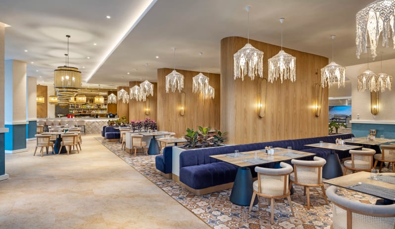 Petra +16 Adult Restaurant Spacious modern restaurant dining room featuring white macramé pendant lights, wood-paneled walls, and deep blue velvet booth seating at Liberty Signa Hotel by Kenwood Travel