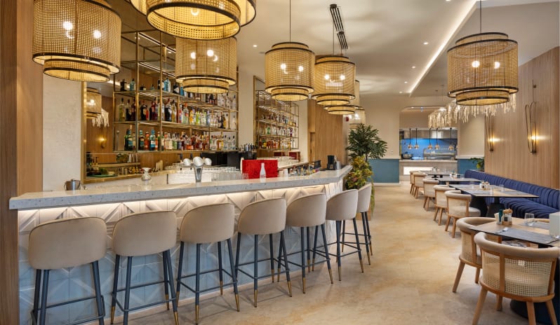 Petra +16 Adult Restaurant interior featuring a white marble bar, woven rattan pendant lights, and plush blue velvet booth seating at Liberty Signa Hotel by Kenwood Travel