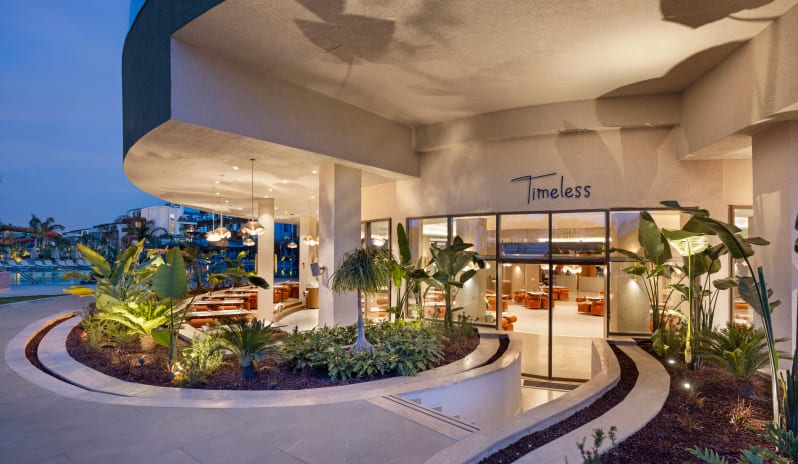 Timeless 7/24 A’la Carte Restaurant Exterior view of Timeless restaurant featuring a modern curved terrace, lush tropical landscaping, and warm ambient lighting at dusk at Liberty Signa Hotel by Kenwood Travel