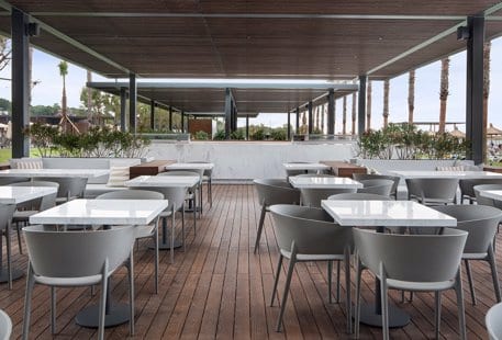 Beach Bar outdoor patio seating at the Voyage Belek Beach Bar featuring white marble tables, grey contemporary chairs, and wooden decking under a shaded pavilion at Voyage Belek Golf & Spa by Kenwood Travel