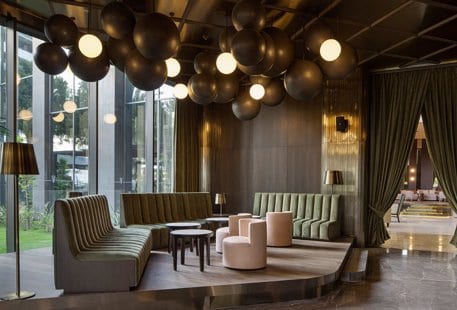 Bloom Bar green velvet fluted sofas, pink barrel chairs, and a unique spherical cluster chandelier at Voyage Belek Golf & Spa by Kenwood Travel