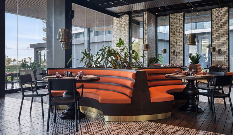 Carino Steak Restaurant curved orange booth seating, designer pendant lights, and patterned floor tiles at Voyage Belek Golf & Spa by Kenwood Travel
