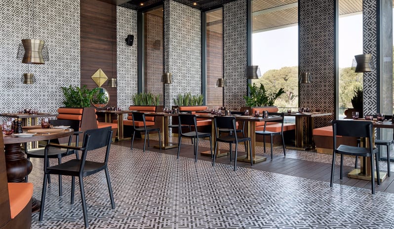 Carino Steak Restaurant geometric patterned walls and floors, orange upholstery, and large windows with garden views at Voyage Belek Golf & Spa by Kenwood Travel