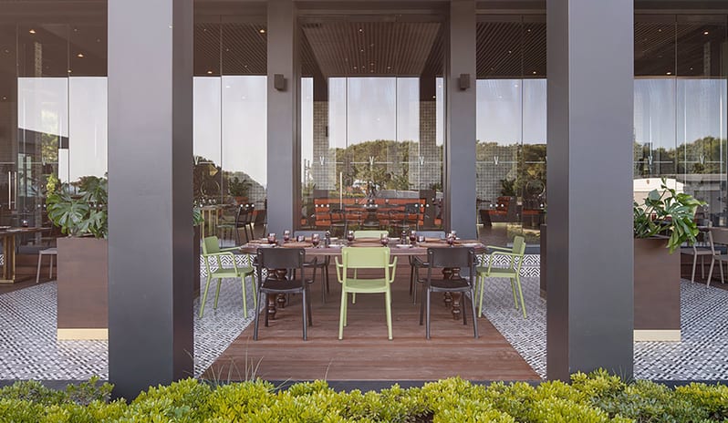 Carino Steak Restaurant a set dining table with lime green and black chairs, wood decking, and large glass windows at Voyage Belek Golf & Spa by Kenwood Travel