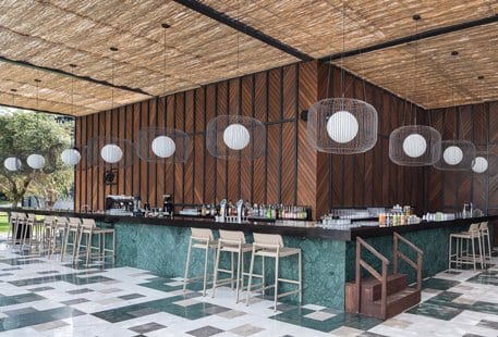 Family Pool Bar green marble counter, wooden chevron wall panels, and globe pendant lighting under a thatched roof at Voyage Belek Golf & Spa by Kenwood Travel