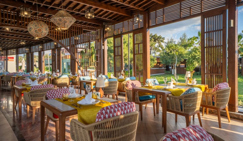 Buddha Indian Restaurant elegant wooden architecture, vibrant yellow table runners, and woven wicker seating overlooking a lush green garden at Liberty Fabay by Kenwood Travel