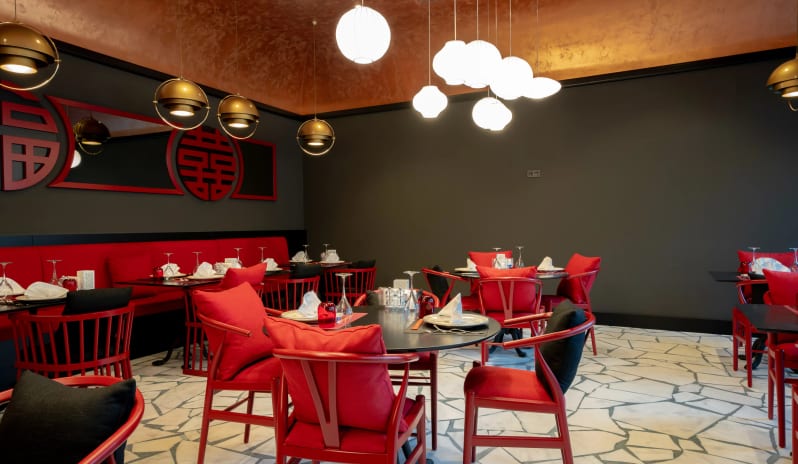 Night Snack modern red wishbone-style chairs, black tables, and large white globe pendant lights against a dark grey wall with traditional Asian decor at Liberty Fabay by Kenwood Travel