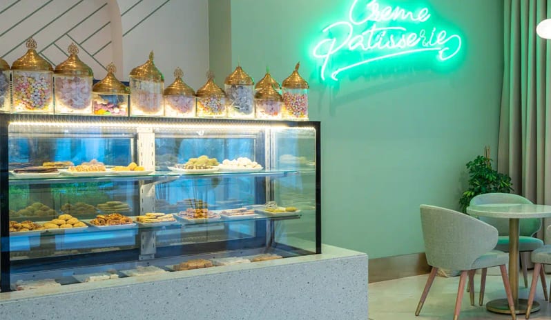 Pisidia Patisserie featuring a neon sign, a display case of Turkish desserts and pastries, and mint green decor at Liberty Fabay by Kenwood Travel