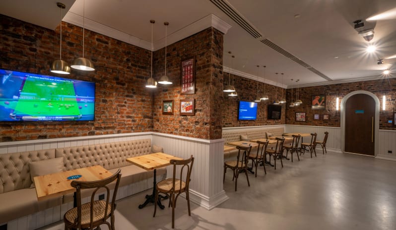 Sports Bar exposed brick walls, tufted banquet seating, wooden tables, and flat-screen TVs showing a snooker match at Liberty Fabay by Kenwood Travel
