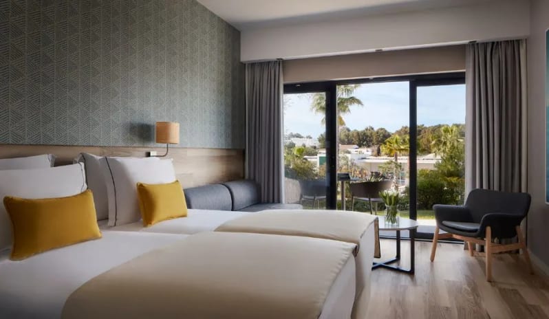 Deluxe Room interior with floor-to-ceiling glass doors leading to a terrace, featuring light wood floors and a contemporary sitting area at Tivoli Alvor Algarve by Kenwood Travel