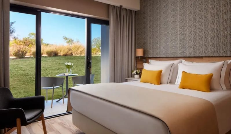 Family Deluxe Room large bed with yellow accents, patterned wallpaper, and a sliding glass door opening to a private garden patio at Tivoli Alvor Algarve by Kenwood Travel