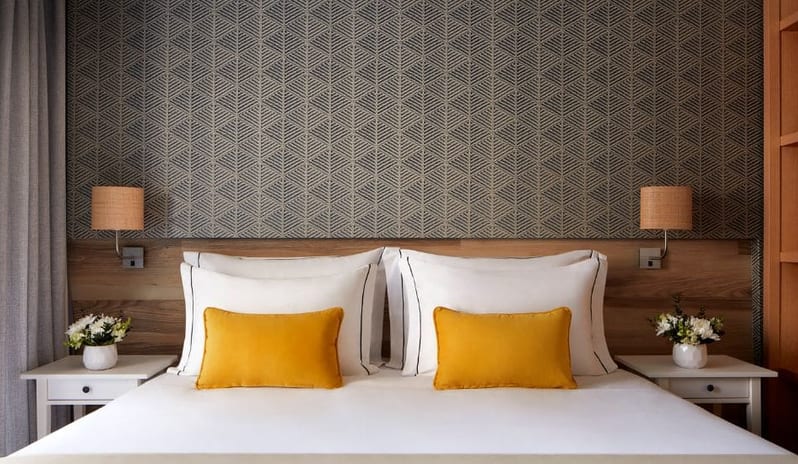 Family Deluxe Room lgeometric patterned headboard, bedside tables with white flowers, and warm wall-mounted lamps at Tivoli Alvor Algarve by Kenwood Travel