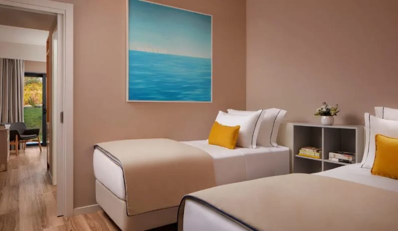 Family Deluxe Room two single beds with yellow pillows, blue ocean-themed wall art, and a view into the main living space at Tivoli Alvor Algarve by Kenwood Travel