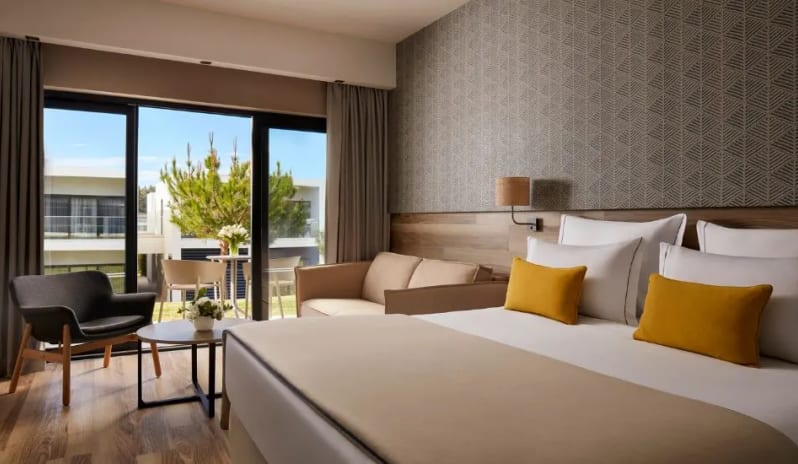 Family Room king bed with yellow accent pillows, a seating area, and large sliding doors opening to a private balcony at Tivoli Alvor Algarve by Kenwood Travel