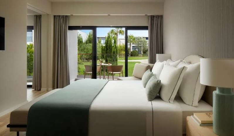 Premium Suite bedroom at Tivoli Alvor Algarve Resort featuring a king-size bed, sea-green accents, and a private balcony overlooking lush gardens at Tivoli Alvor Algarve by Kenwood Travel