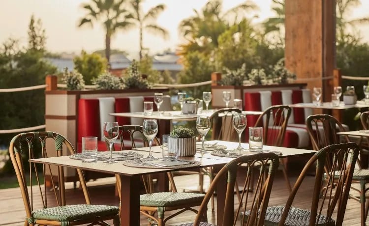 Mad Med wooden tables, wicker chairs, and red-and-white striped booths at sunset at Tivoli Alvor Algarve by Kenwood Travel