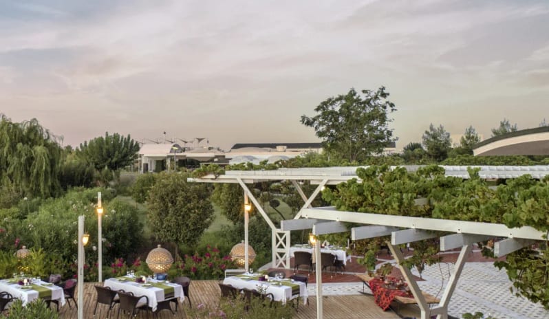 A la Turca Turkish Restaurant white pergolas, set tables with green runners, and lush garden surroundings at sunset at Hilton Dalaman Sarigerme Resort & Golf by Kenwood Travel