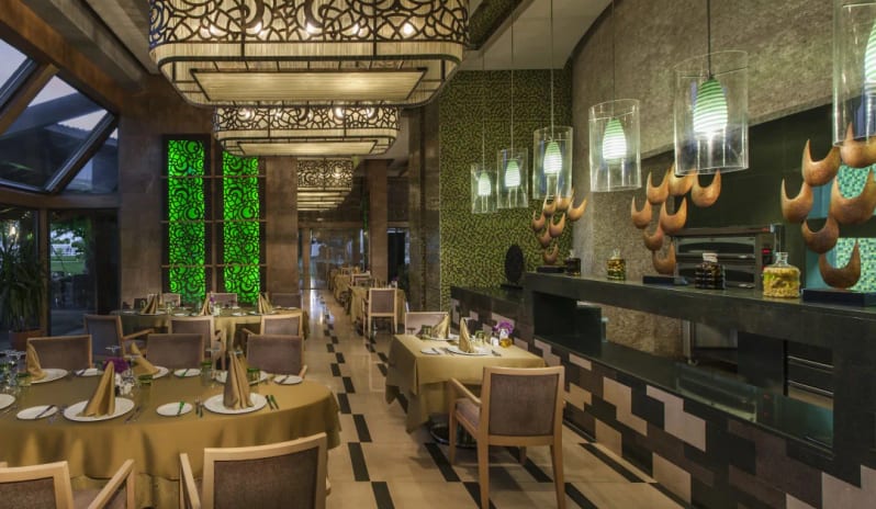 Alize Italian Restaurant ornate filigree pendant lights, set dining tables, and a modern open kitchen counter. at Hilton Dalaman Sarigerme Resort & Golf by Kenwood Travel