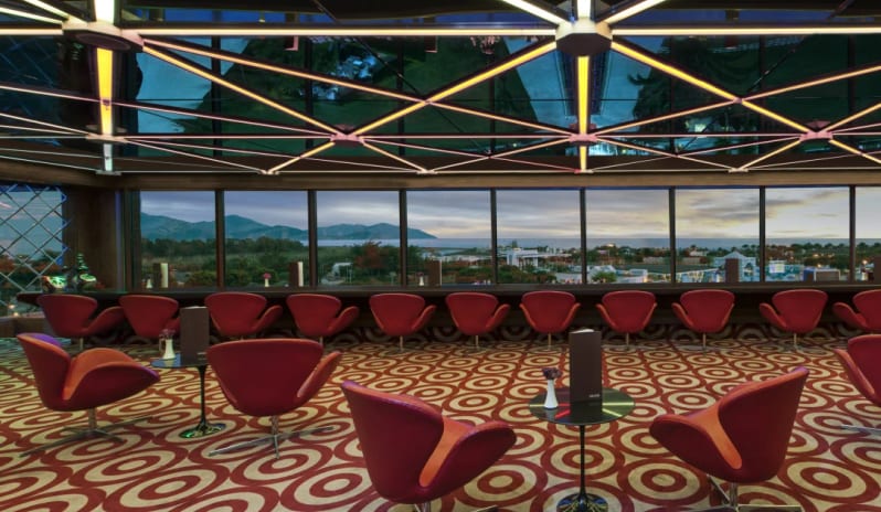 Rouge Roof Bar red swan chairs, patterned carpets, and a geometric light installation with a sunset mountain view at Hilton Dalaman Sarigerme Resort & Golf by Kenwood Travel