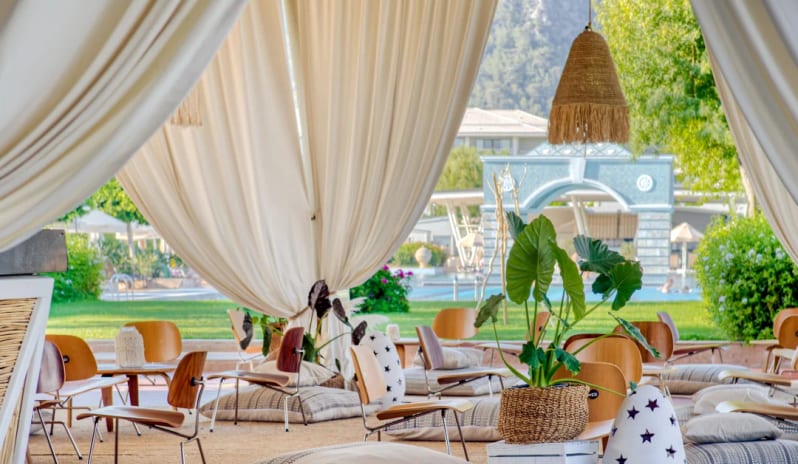 Vento Snack & Bar bohemian decor, floor cushions, Eames-style chairs, and white draped curtains overlooking the resort pool and gardensat Hilton Dalaman Sarigerme Resort & Golf by Kenwood Travel