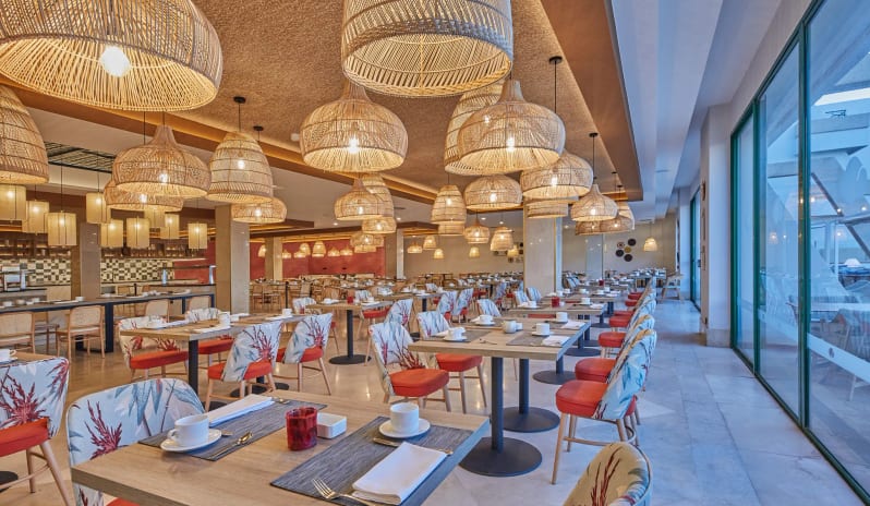 World Cafe restaurant dining area featuring tables with red floral patterned chairs and numerous large woven wicker pendant lights at Dreams Lanzarote Playa Dorada Resort & Spa by Kenwood Travel