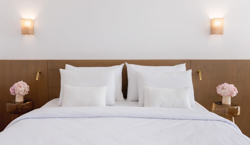 LUX ME Panoramic Guestroom Sea View Luxury king bed with crisp white linens and pink floral arrangements at Grecotel LUXME Dama Dama by Kenwood Travel